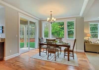 A bright dining area with large windows, a wooden table set, and a sliding glass door leading to a garden.