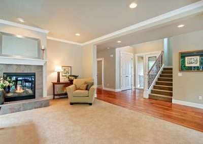 A bright and spacious living room featuring a cozy fireplace, a beige armchair, and a staircase leading to the upper floor.