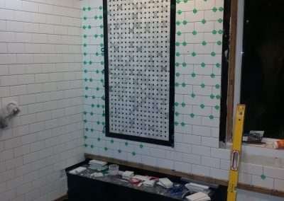 Partially completed bathroom wall tiling showing a black and white woven pattern in the center, surrounded by white subway tiles.
