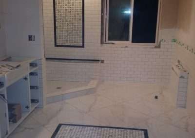 A fully tiled bathroom featuring a mosaic tile floor centerpiece and white subway tiles on the walls, with marble accents throughout.