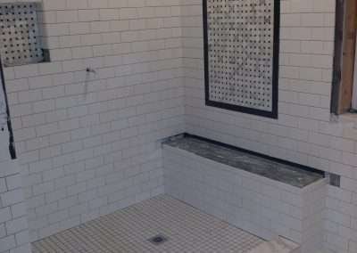 A modern shower enclosure with white subway tiles, a mosaic accent on the wall, and a small bench along one side.