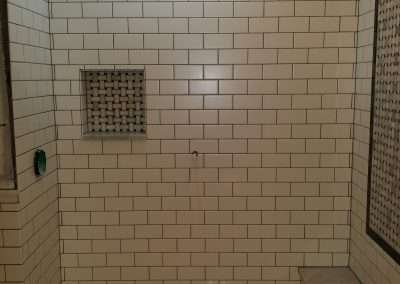 A stylish shower with white subway tiles, a mosaic accent wall, and a built-in niche for storage.