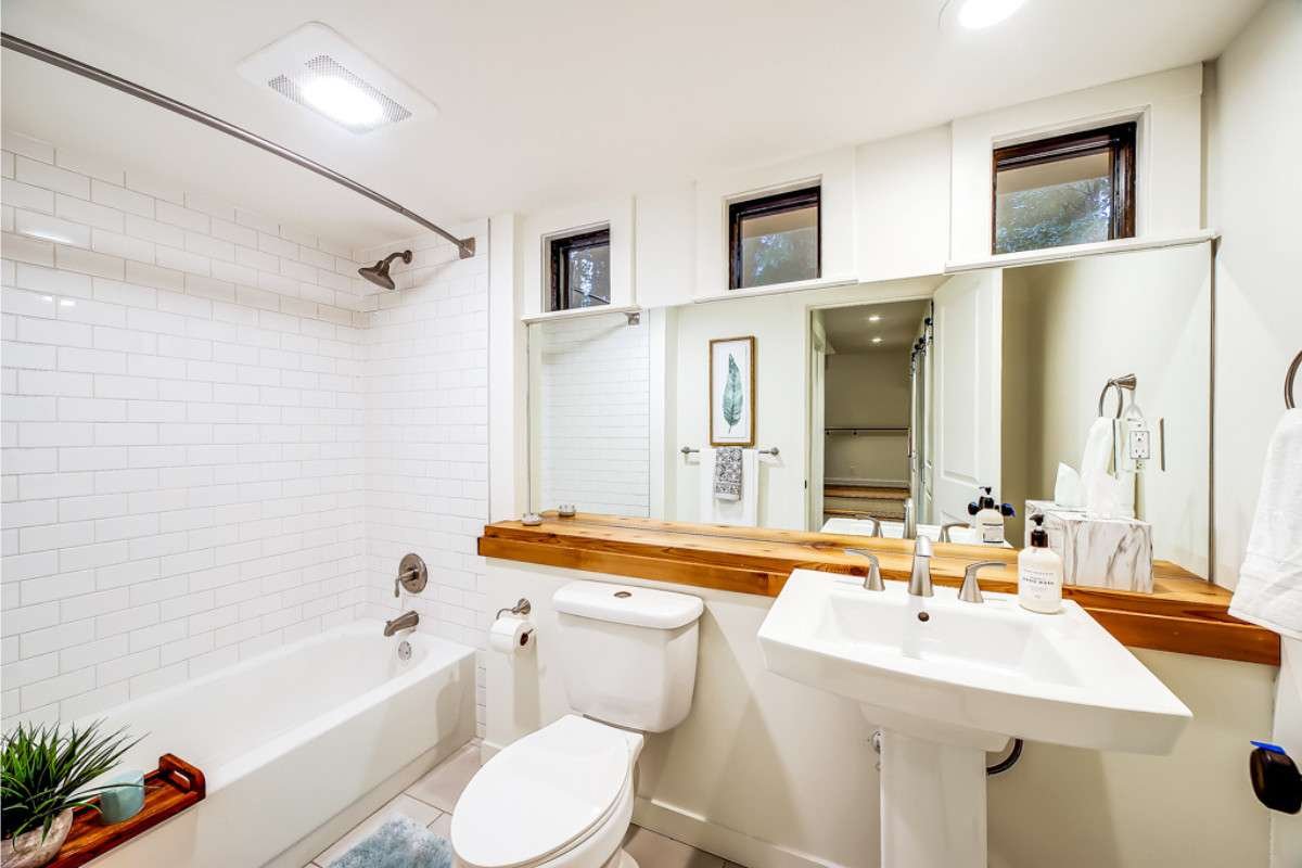 Bright white bathroom featuring subway tile, pedestal sink, wood countertop, and transom windows