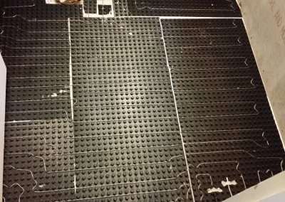 Basement floor with black waterproofing membrane and radiant heating system.