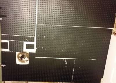 Basement wall with black waterproofing membrane and plumbing fixtures.