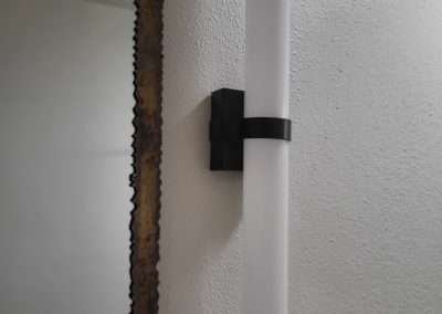 A close-up view of a modern bathroom light fixture with a cylindrical frosted glass design mounted next to a textured mirror frame.