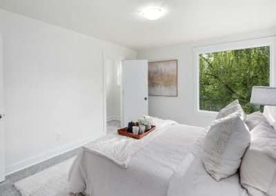 A cozy bedroom with a neatly made bed, featuring a tray with coffee cups and flowers, and a large window showcasing a scenic view.
