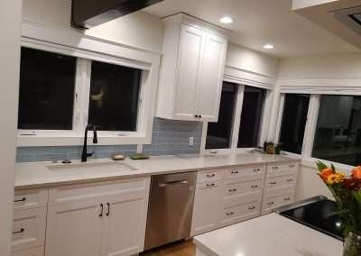 A bright kitchen featuring a long countertop with white cabinets and large windows.
