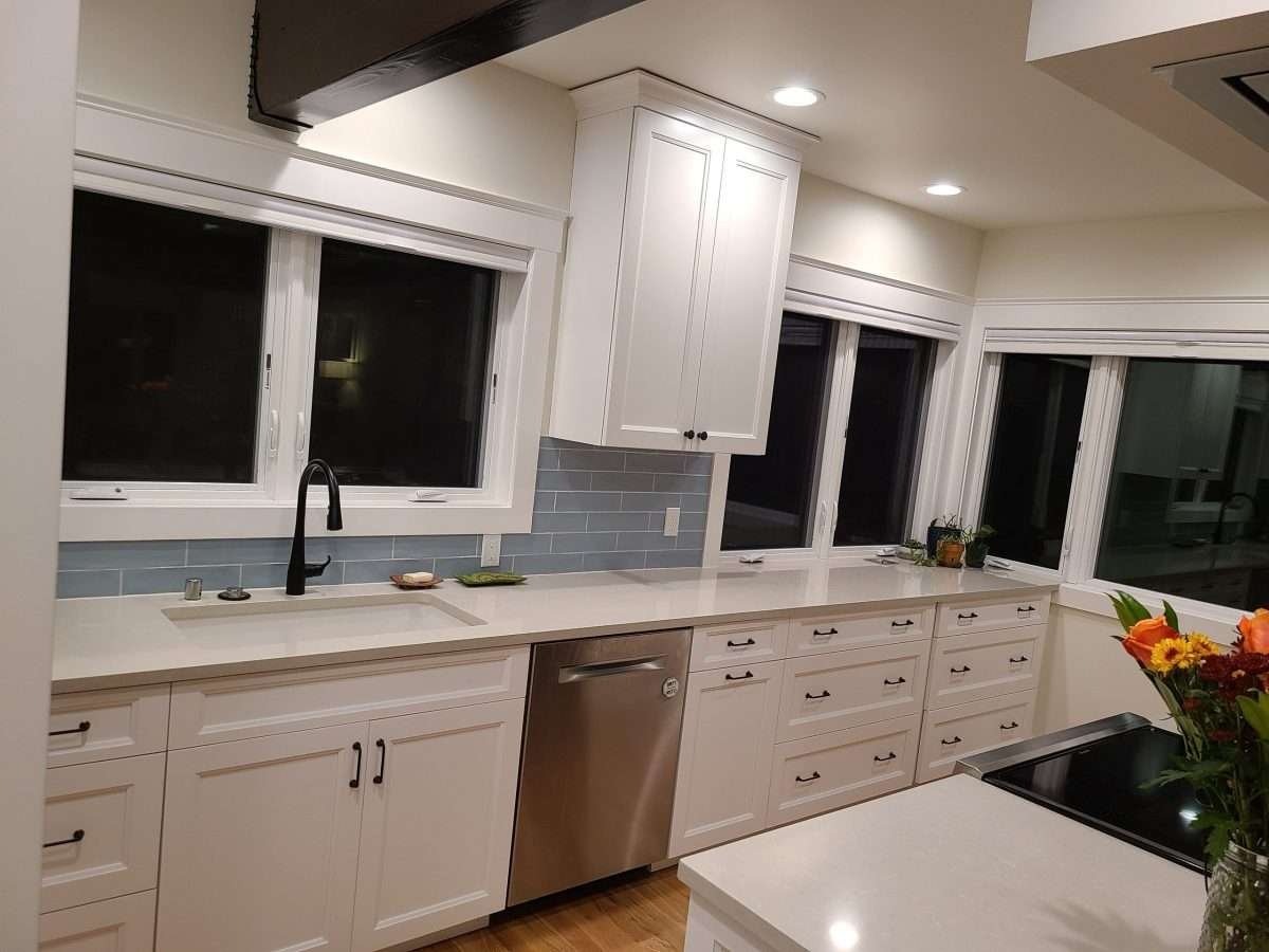 A bright kitchen featuring a long countertop with white cabinets and large windows.