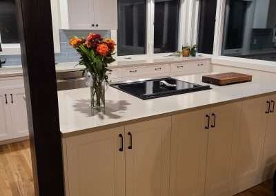 A bright kitchen with an island, white cabinets, and large windows allowing natural light to enter.