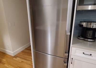 A sleek, built-in stainless steel refrigerator integrated into a modern kitchen with white cabinetry.