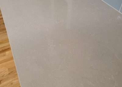 A detailed close-up of a sleek, modern kitchen countertop with a light gray surface, complemented by a blue subway tile backsplash and hardwood floors.