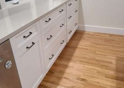 A contemporary kitchen featuring sleek white cabinets, a large island, and wood flooring.