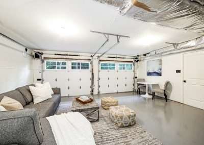 A cozy basement lounge area with a sectional sofa, ottomans, and a table, featuring ductwork and ample lighting.