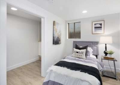 A small bedroom with a neatly made bed, lamp, and a window providing natural light.