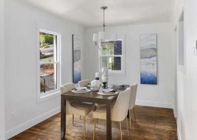A bright dining area with a wooden table set for four, modern artwork on the walls, and large windows providing natural light