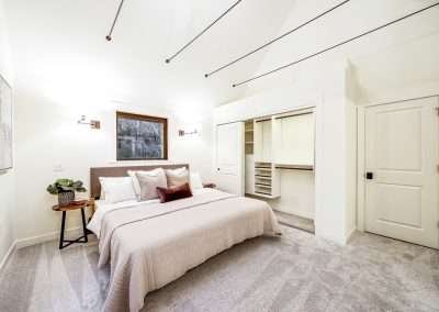 A master bedroom with a large bed, bedside tables, and windows overlooking the forest, featuring soft carpeting.