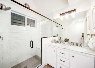 A modern bathroom with a large glass-enclosed shower, double sink vanity, and white tile walls.