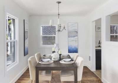 A tastefully decorated dining room with a wooden table, beige chairs, modern chandelier, and contemporary artwork.