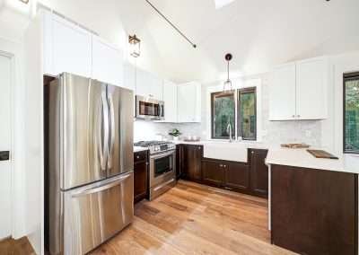 A modern kitchen with white cabinets, stainless steel appliances, and dark wood flooring, featuring ample natural light.