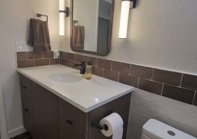 A full view of a bathroom showing a vanity, toilet, bathtub with clear shower curtain, and a glass block window.