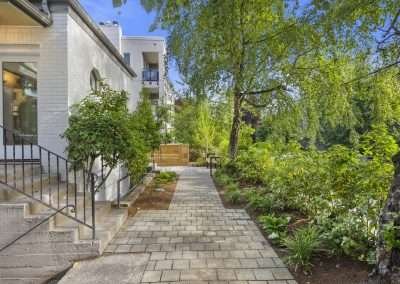 A newly renovated front pathway with brick paving, lush greenery, and a modern white brick exterior of the home