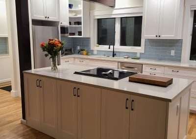 A functional kitchen island with a built-in cooktop, white cabinets, and a vase of flowers.