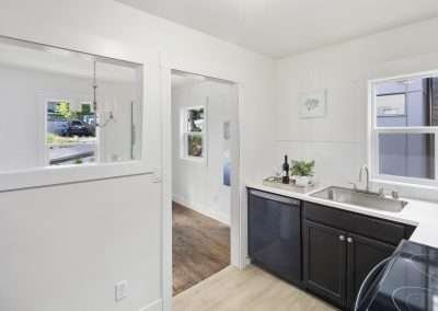 A functional kitchen area with dark cabinets, a sink, dishwasher, and a view into the dining room.