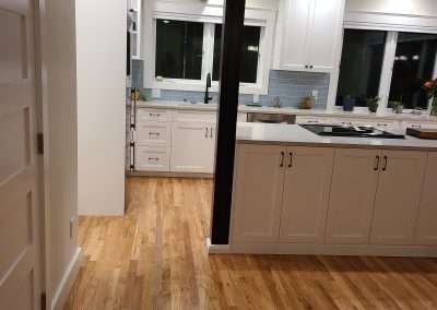 A view from the hallway into a modern kitchen with clean lines, white cabinets, and warm hardwood floors.