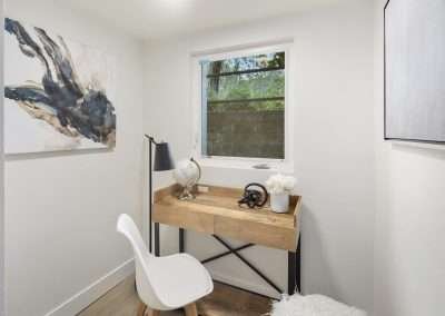 A small home office nook with a desk, chair, lamp, and decorative artwork.