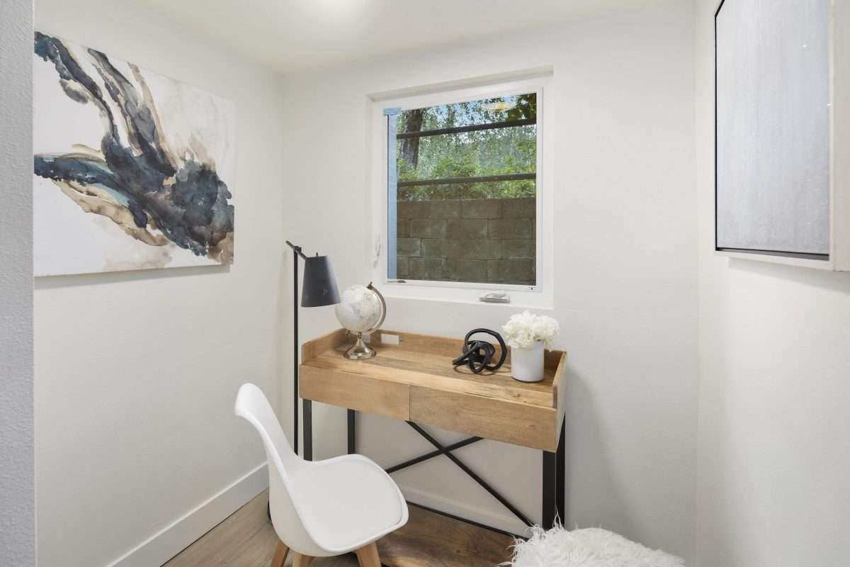 A small home office nook with a desk, chair, lamp, and decorative artwork.