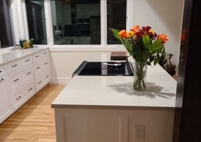 A kitchen island with a built-in cooktop, white cabinets, and a vase of flowers.