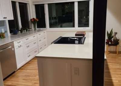 A modern kitchen island with a white countertop, black accents, and an integrated cooktop, surrounded by white cabinets and hardwood floors.