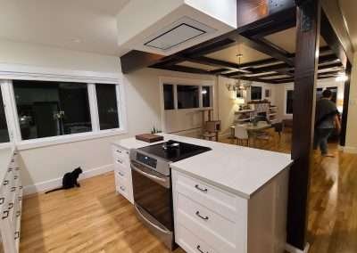 A modern kitchen with an adjacent dining area, featuring a black and white theme, hardwood floors, and a central island with an integrated cooktop.