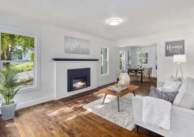 A modern living room with white walls, a cozy fireplace, wooden floors, and stylish furnishings