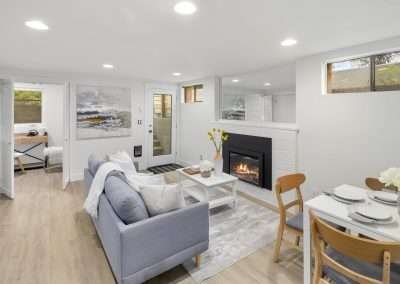 A view of the living area with a sofa, coffee table, fireplace, and dining table in the background.