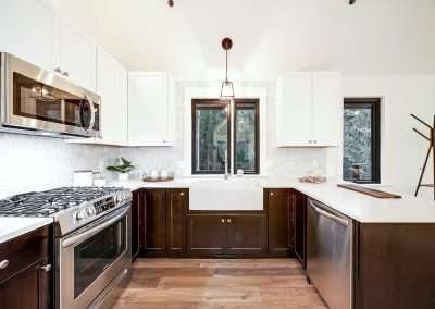 A modern farmhouse kitchen featuring stainless steel appliances, white and dark wood cabinets, a farmhouse sink, and a large window overlooking greenery.