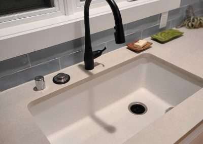 A stylish modern kitchen sink with a black faucet, set against a white countertop and white cabinets.
