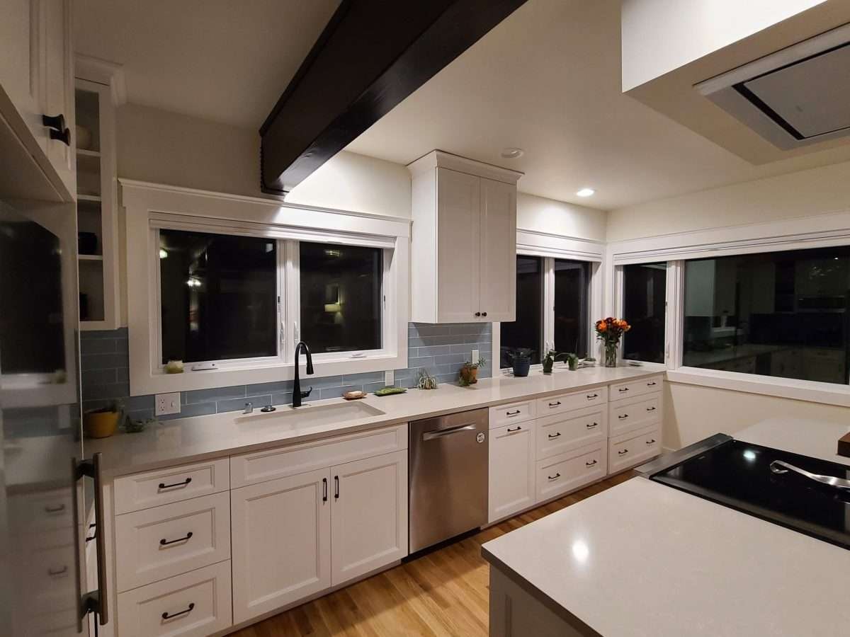 A modern kitchen with large windows, a sleek black faucet, white cabinetry, and an open layout, perfect for a bright and inviting space.