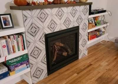 Modern living room featuring a stylish fireplace with decorative tiles and a mounted TV above, surrounded by bookshelves.