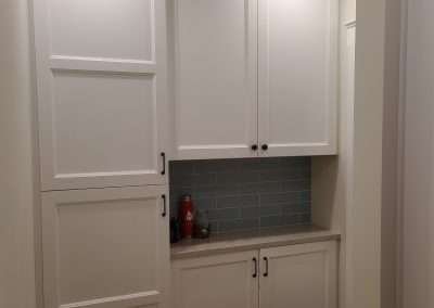 A modern pantry storage area in a kitchen, featuring tall white cabinets and a countertop with a backsplash.