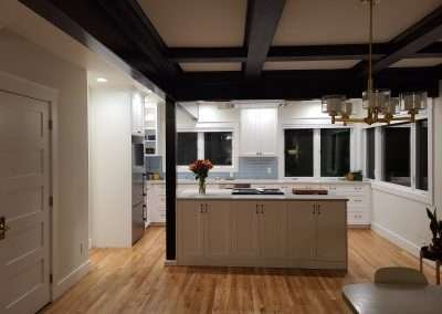An open concept kitchen with a large island, white cabinets, and dark ceiling beams.