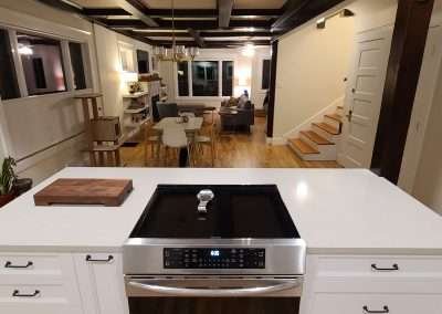 An open concept kitchen and living area showcasing a central kitchen island with a stove, white cabinets, and a view into the dining and living spaces.