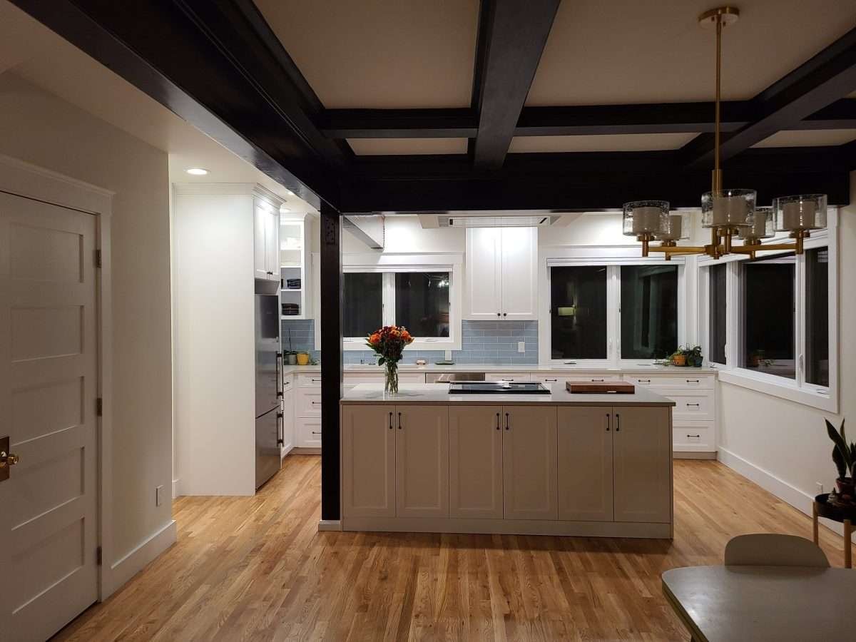 An open concept kitchen with a large island, white cabinets, and dark ceiling beams.
