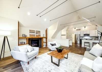 An open concept living room with a high ceiling, modern furniture, and a fireplace, leading to the kitchen.