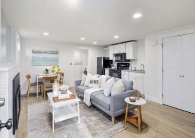 A modern open-plan living area with a cozy sofa, fireplace, dining table, and kitchen in the background.