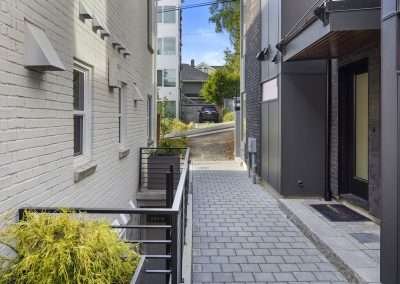 A rear view of the renovated home with modern fencing, a paved walkway, and adjacent structures