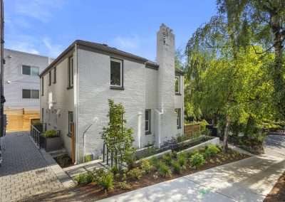 A side entrance to the home with brick paving, modern light fixtures, and a small garden area