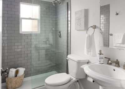 A stylish bathroom with patterned floor tiles, a glass shower, white fixtures, and grey subway tiles