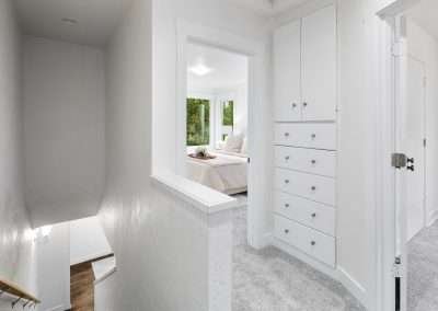An upstairs hallway with wooden floors, white walls, and modern light fixtures
